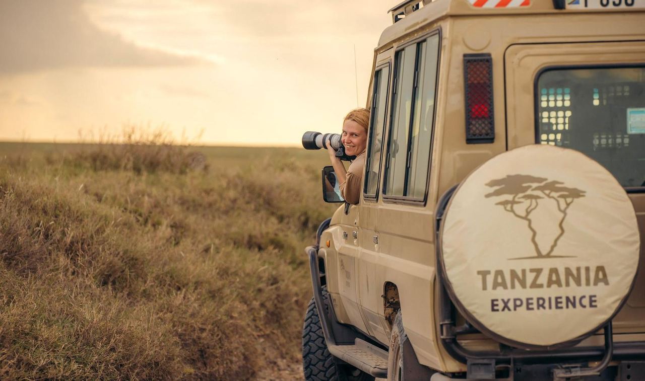Frau mit Kamera am Beifahrersitz in einem Safarifahrzeug von Tanzania Experience