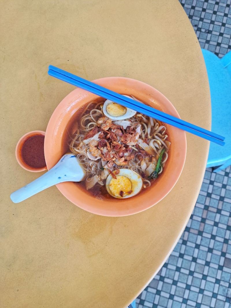 Eine Schale mit malaysischer Laksa-Suppe und blauen Essstäbchen auf einem runden Tisch